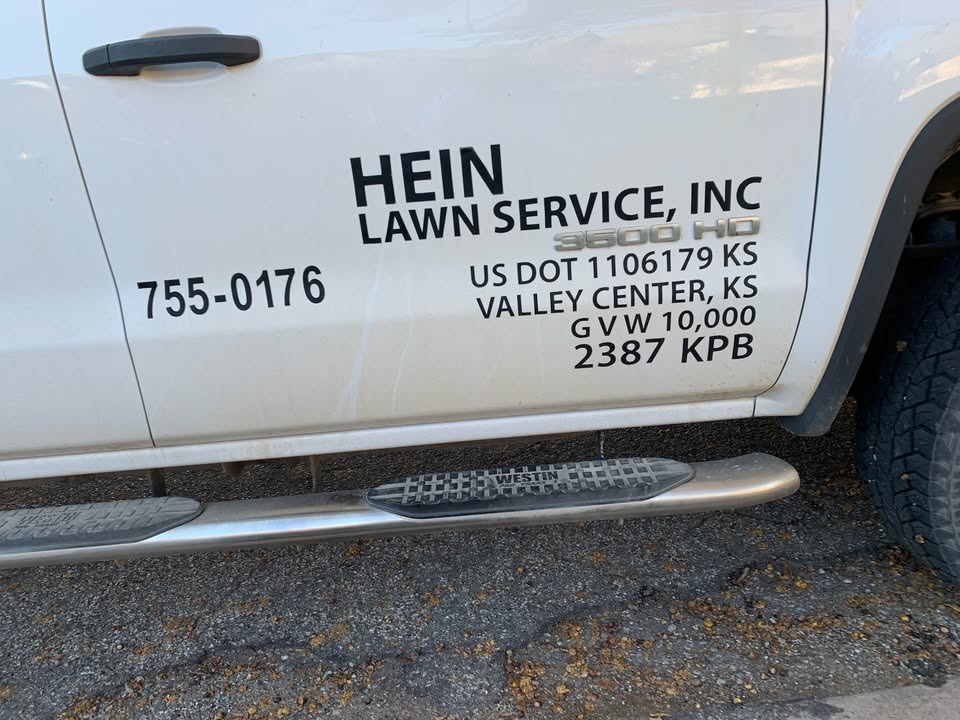 Door of a white Hein Lawn Service pickup truck showing the phone number 755-0176, Valley Center, KS and license number 2387 KPB
